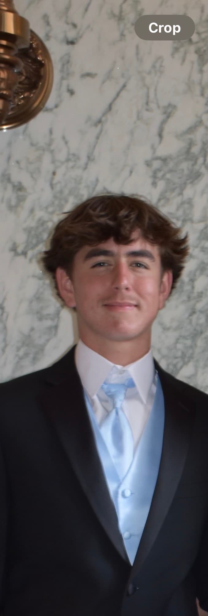Young man with brown hair in a black tuxedo, light blue vest, and matching tie.